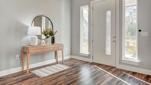 A hallway with a wooden console table, a mirror, and a vase with flowers. There are two doors with windows, and a rug on the floor. - Next to Rainey St, Town Lake, Super Cozy with Modern Aesthetic (Austin)