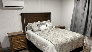 Un dormitorio con cabecera de madera, una cama grande con ropa de cama estampada, dos mesitas de noche y un aire acondicionado instalado en la pared.