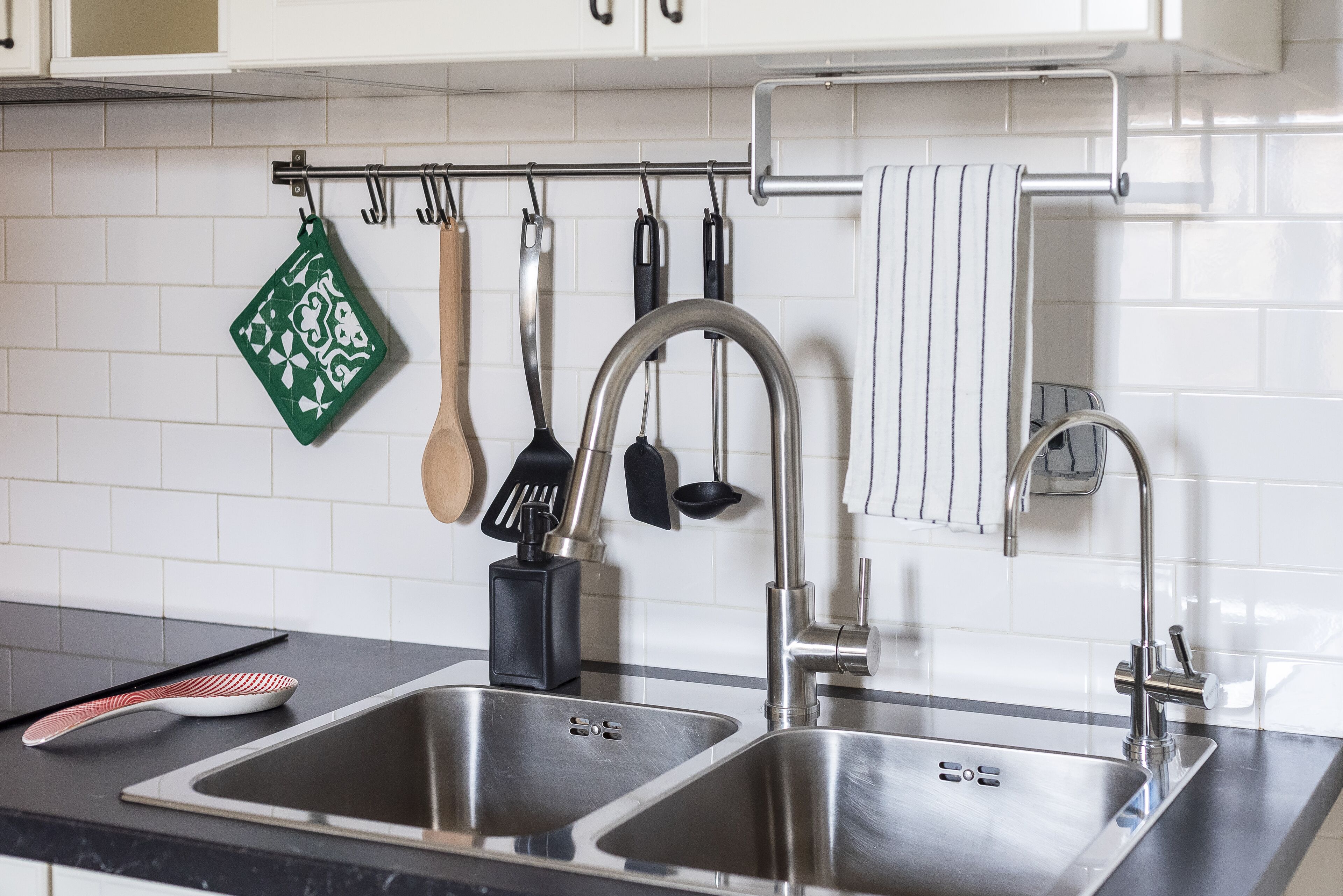 A modern kitchen with two stainless steel sinks, a hanging utensil rack, and a black soap dispenser.