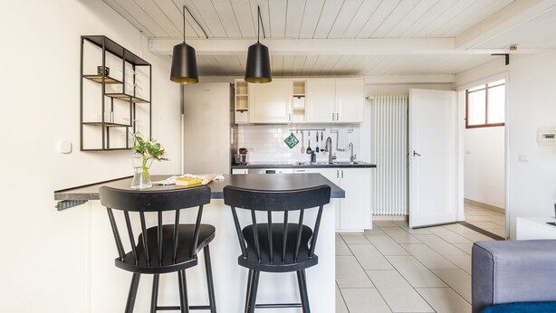 Una cocina moderna con armarios blancos, una isla central y dos taburetes negros.