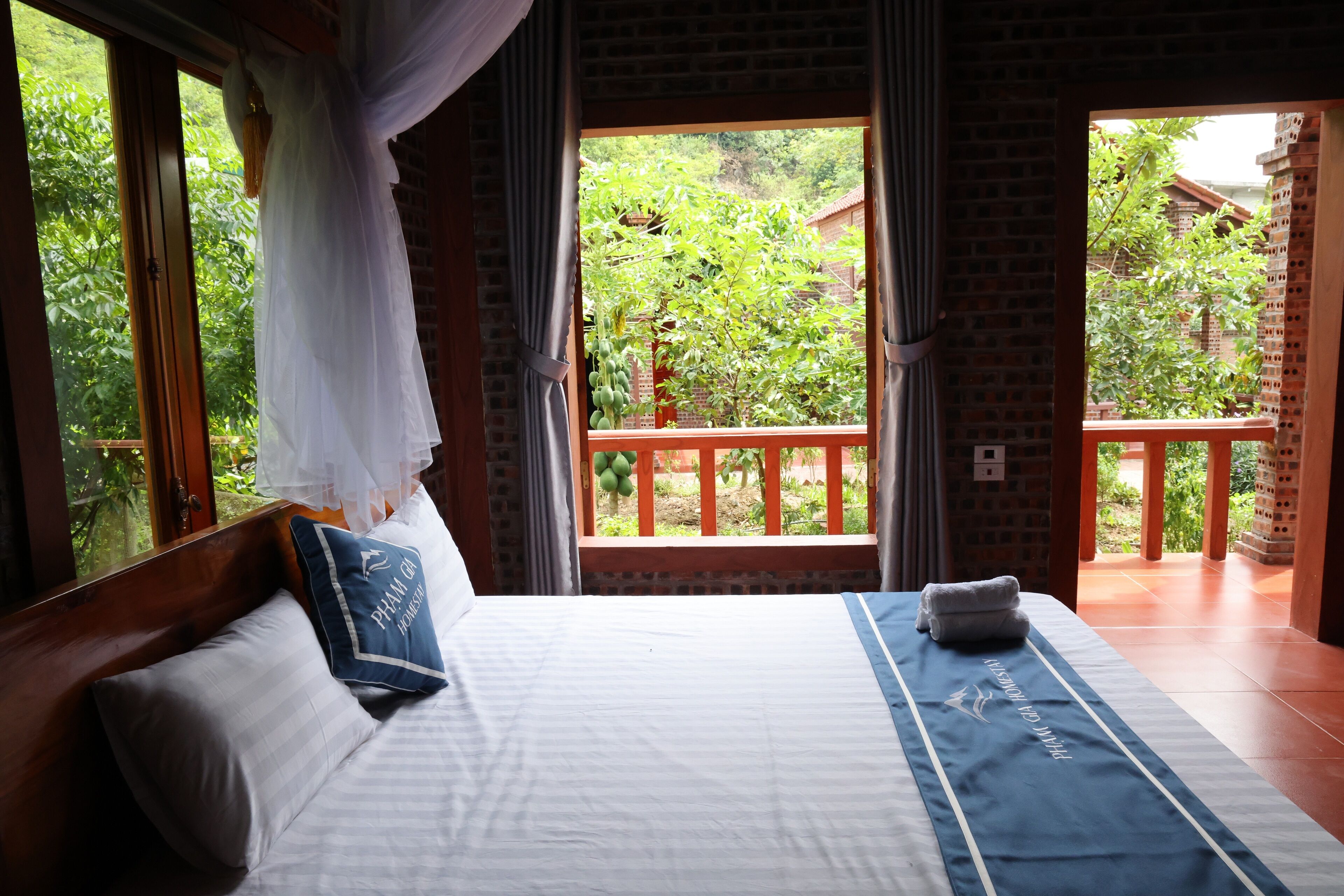 A bedroom with a large bed, a view of a garden through a window, and a balcony with a wooden railing.