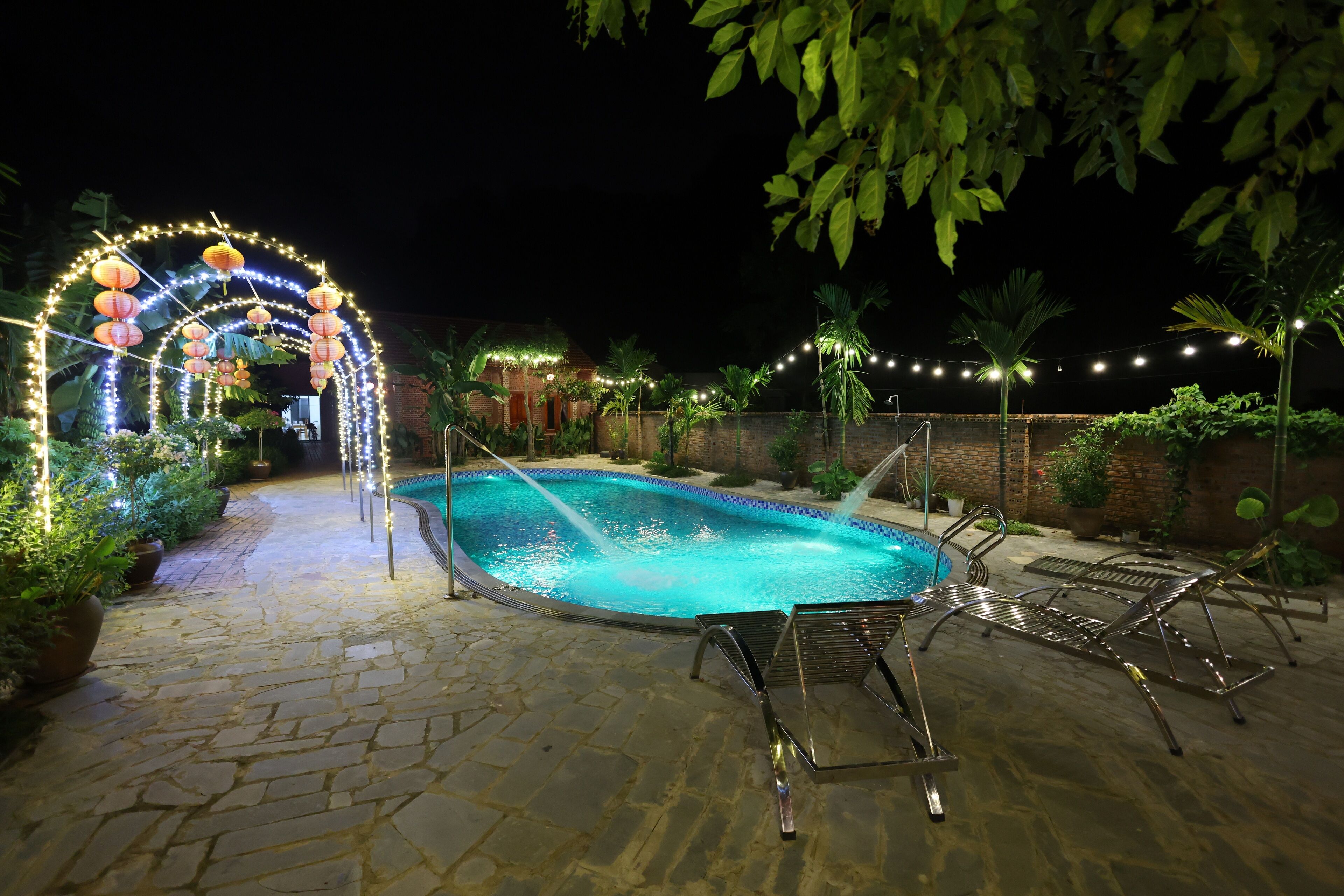 A nighttime pool area with stone flooring, lounge chairs, and string lights.