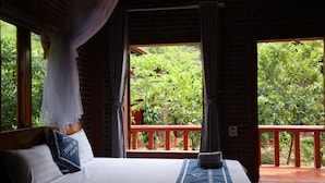 A bedroom with a bed, pillows, and a view of greenery outside.