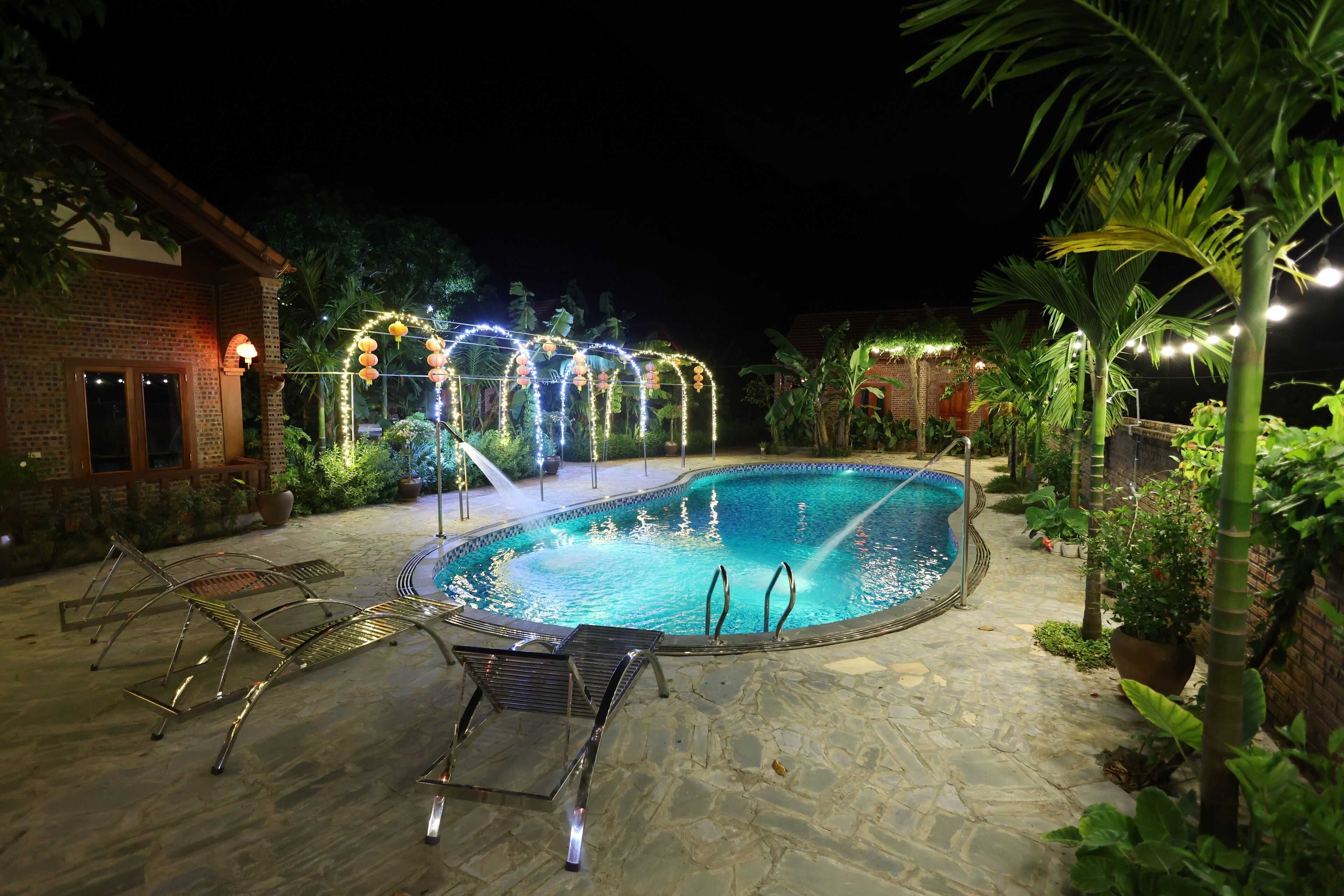 A swimming pool with a stone deck, surrounded by potted plants and a brick building.