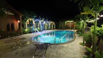 A swimming pool with a stone deck, surrounded by potted plants and a brick building.