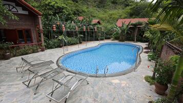 A swimming pool with stone tiles, metal loungers, and a brick building with a red roof.
