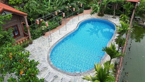 A swimming pool surrounded by lush greenery and traditional buildings with red-tiled roofs.