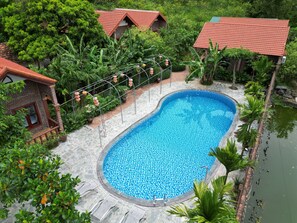 Piscina rodeada de abundante vegetación y edificios tradicionales con tejados rojos.