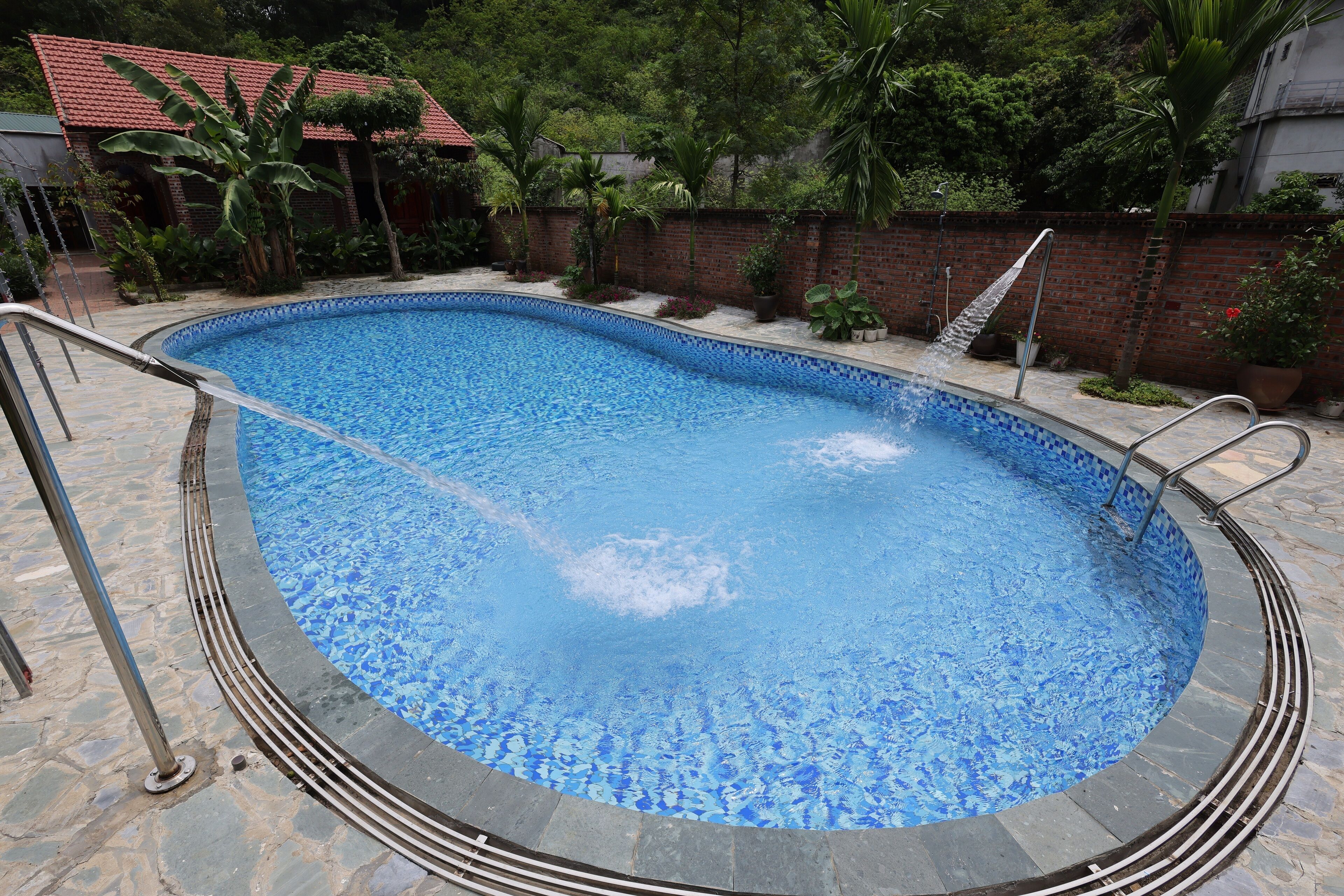 Una piscina con borde de azulejos, rodeada por un solárium de piedra y un muro de ladrillo.