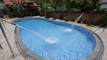 Una piscina con borde de azulejos, rodeada por un solárium de piedra y un muro de ladrillo.