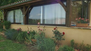 A house with a large window, a balcony with potted plants, and a garden with various flowers and plants. - Country house close to town: 1 star (SARLAT)