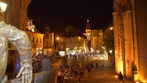 A bustling nighttime street scene with historic buildings, a prominent statue, and people walking and socializing. - Country house close to town: 1 star (SARLAT)