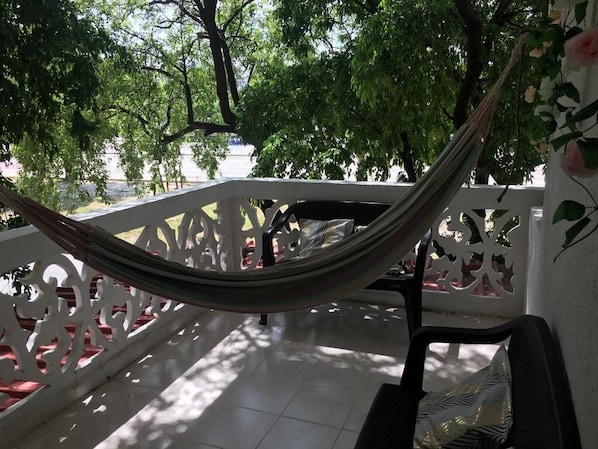 A hammock tied between white lattice railings, a black chair, and a white wall with a floral pattern. - samalinda (Santa Marta)