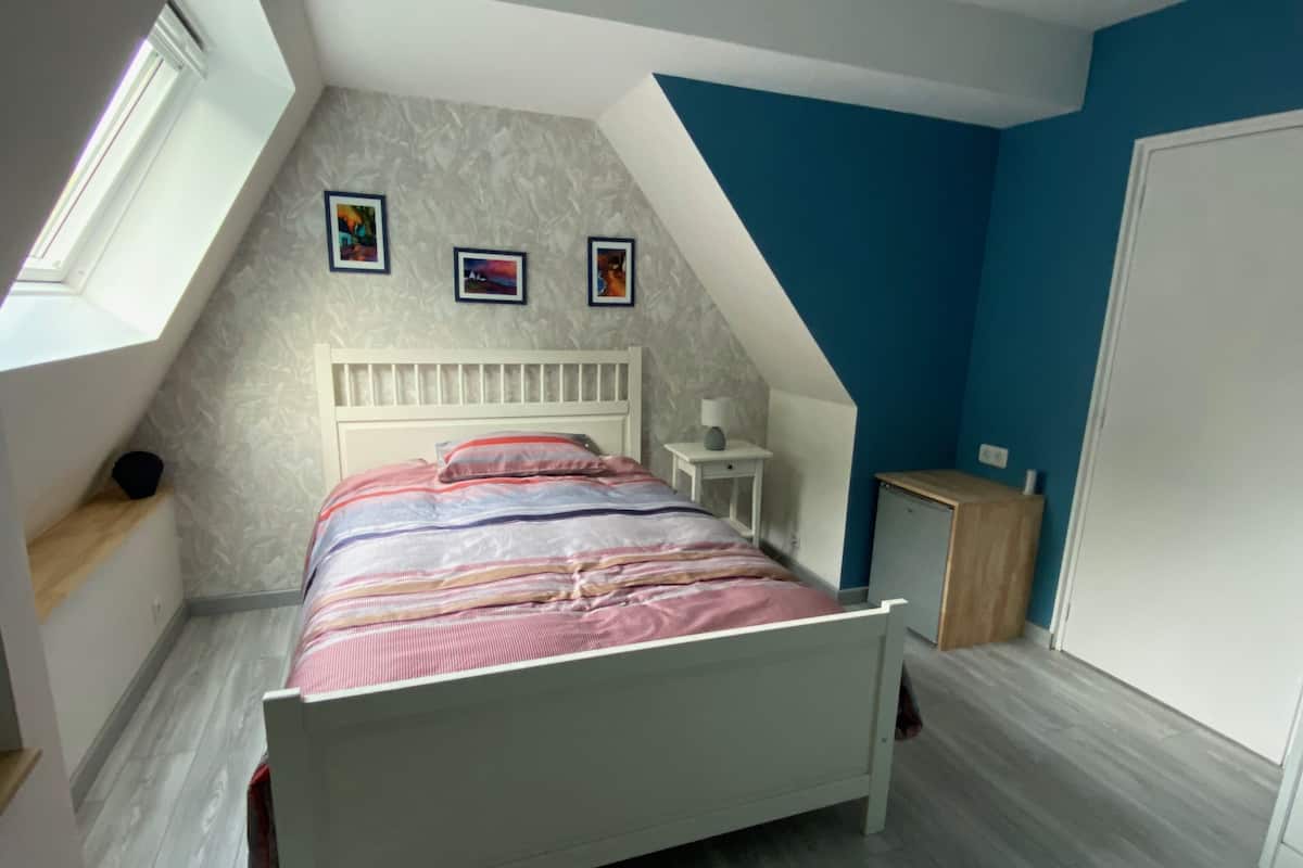 Un dormitorio con techo inclinado, una cama, una mesita de noche, un aparador y una ventana.