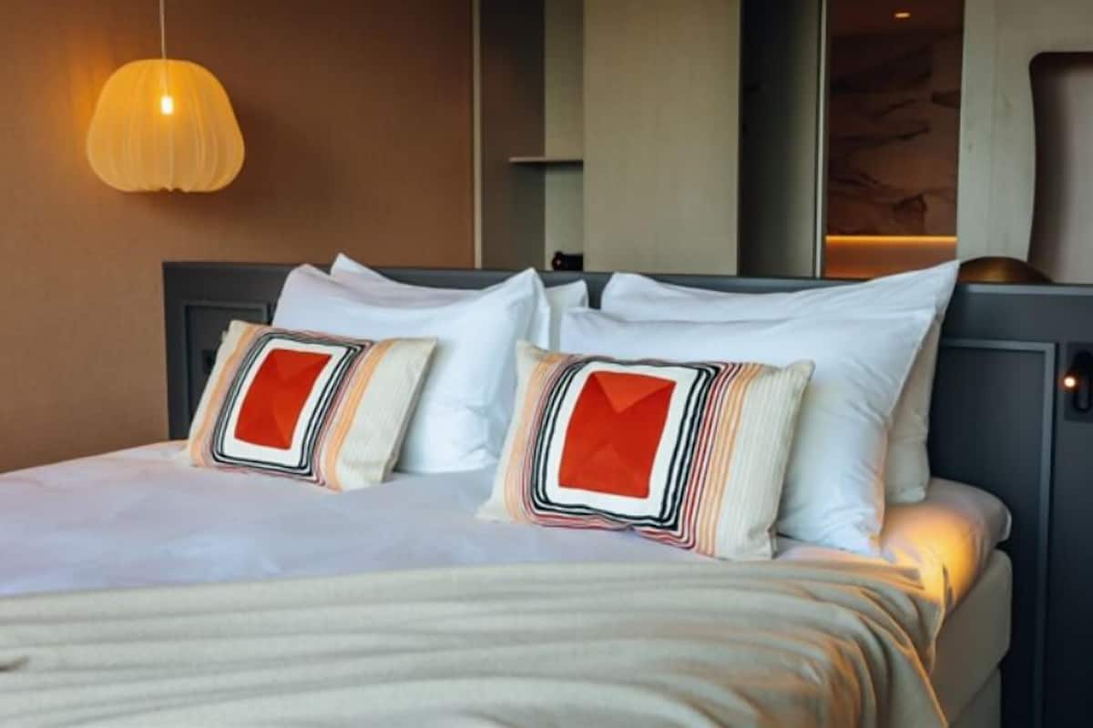 Une chambre d’hôtel équipée d’un lit, d’oreillers, d’un luminaire suspendu et d’un panneau de commande fixé au mur.