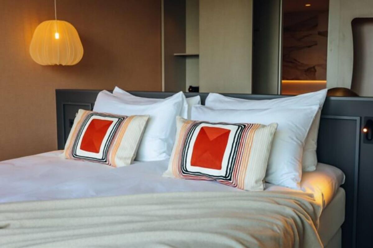 Une chambre d’hôtel équipée d’un lit, d’oreillers, d’un luminaire suspendu et d’un panneau de commande fixé au mur.