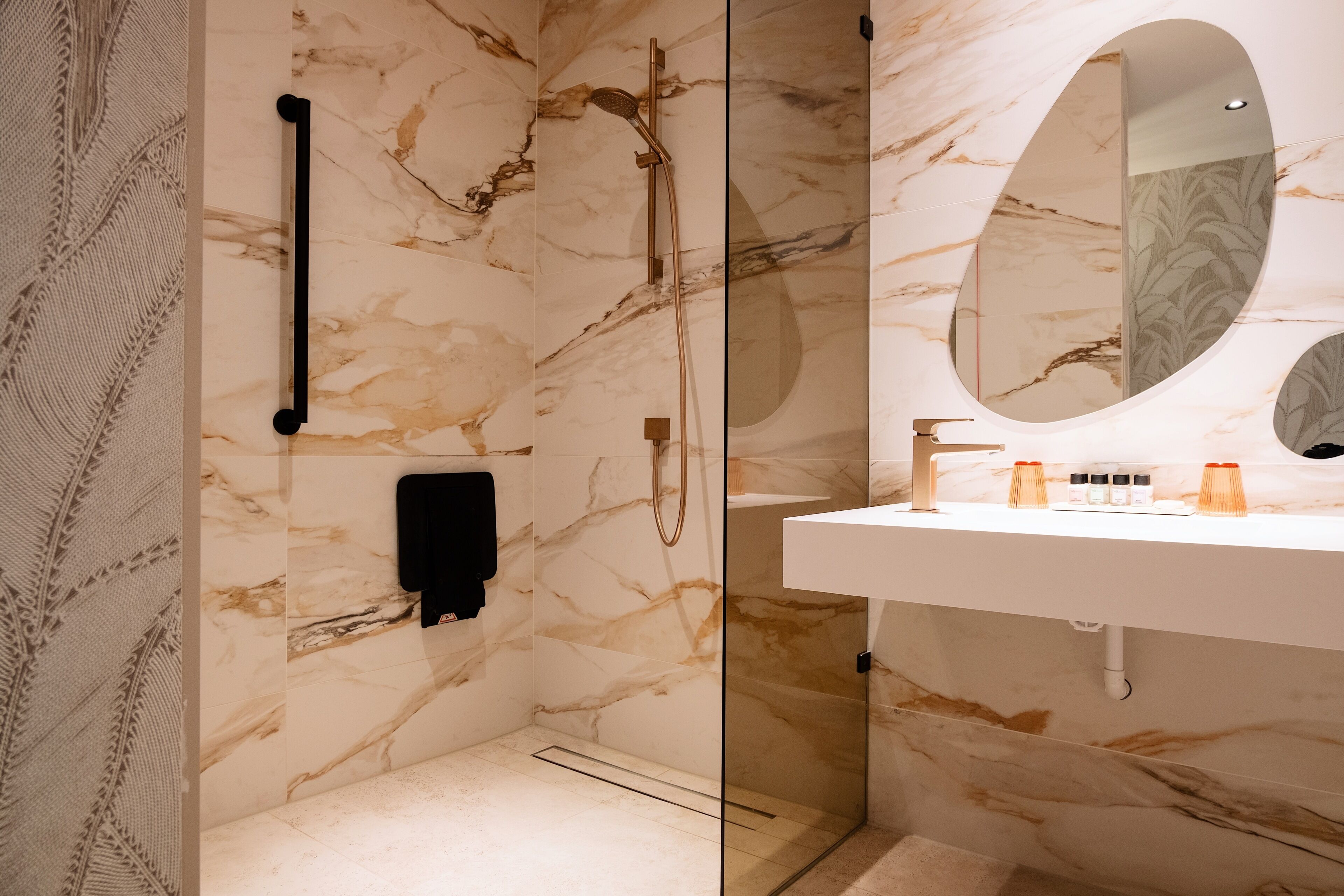 A modern bathroom with marble walls, a glass shower enclosure, and a white sink with a mirror.