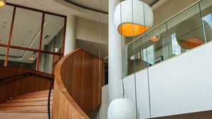 Un interior moderno con una escalera curva, barandillas de madera e iluminación colgante.