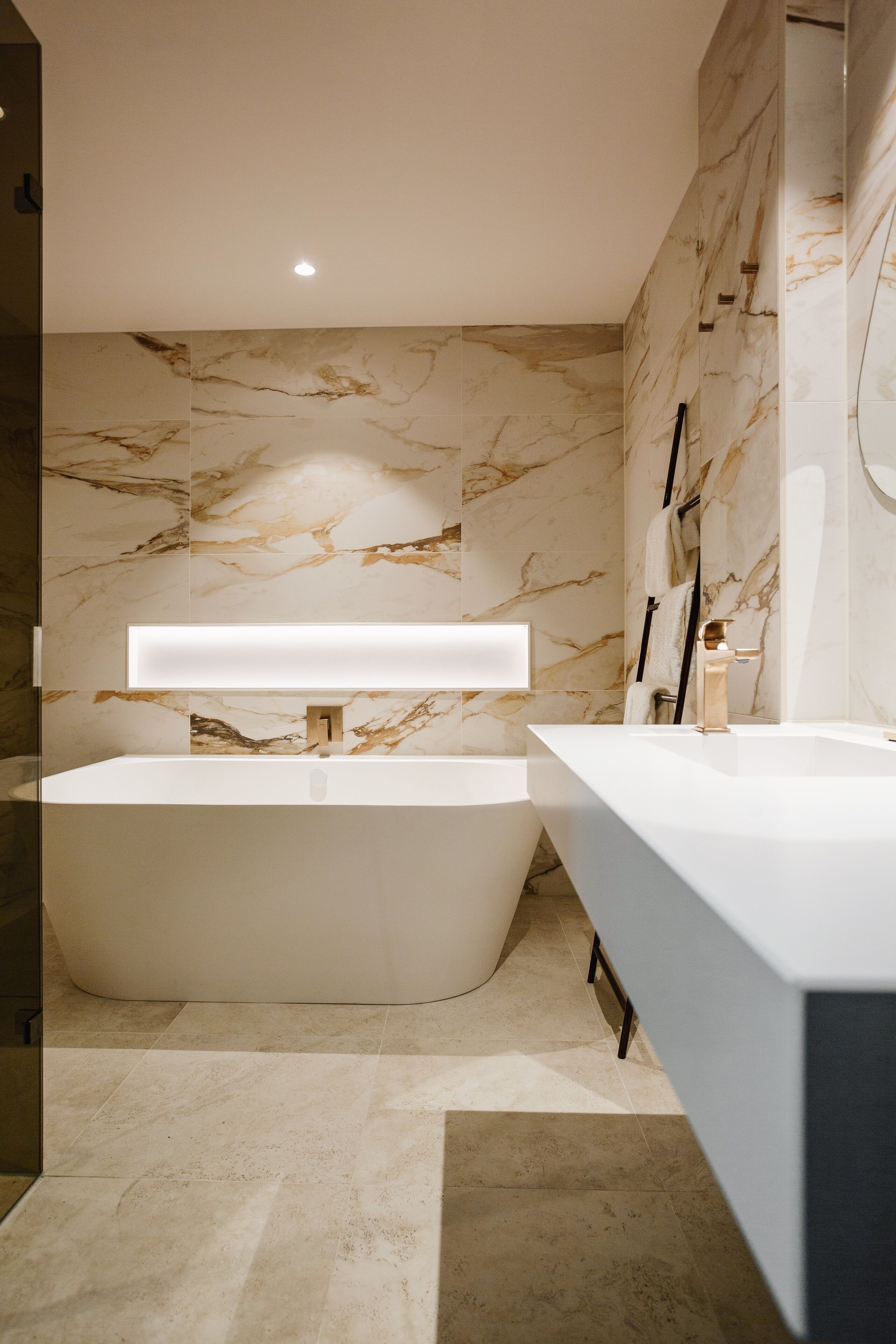 Un baño moderno con una bañera independiente, un lavabo aparte y paredes de mármol.