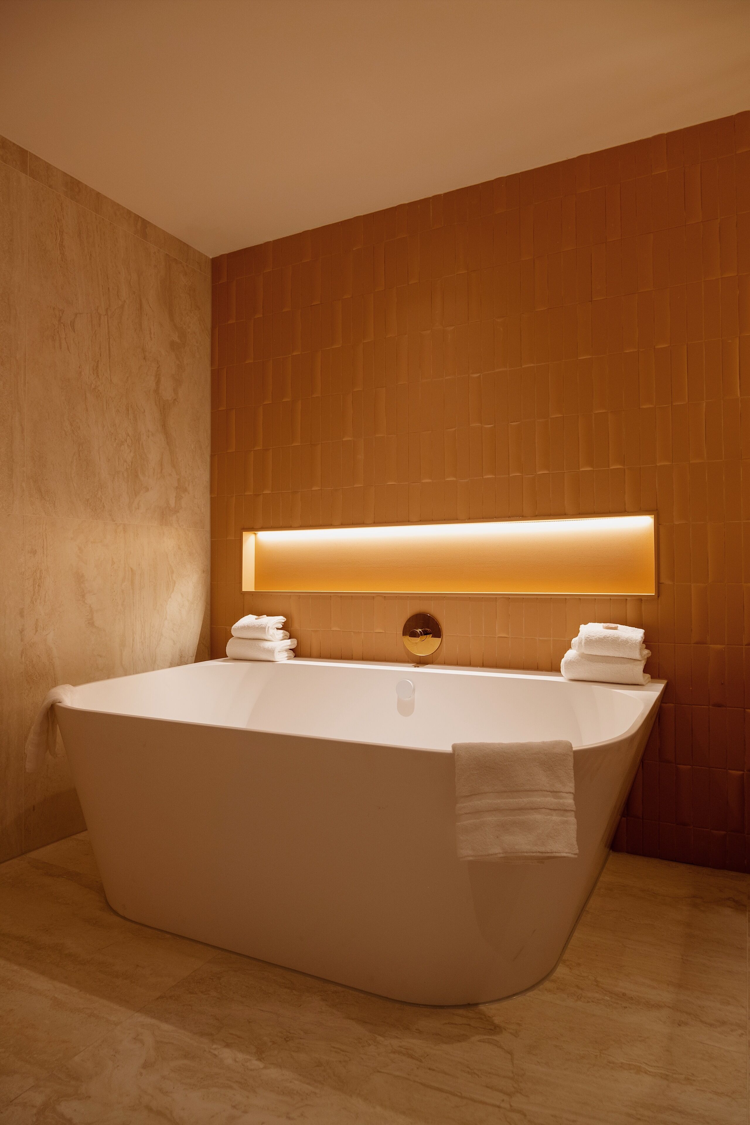 Een moderne badkamer met een vrijstaand bad, een wandlamp en netjes opgevouwen handdoeken.