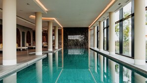 Una piscina interior larga con agua cristalina, rodeada de columnas y amplias ventanas.