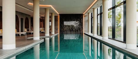 Una piscina interior larga con agua cristalina, rodeada de columnas y amplias ventanas.