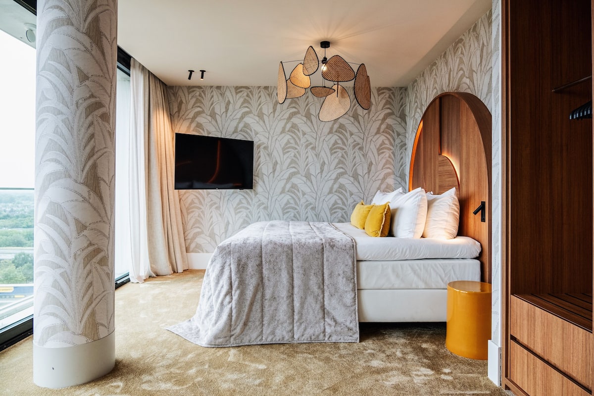 Une chambre avec un lit, une télévision, un luminaire au plafond original et une vue par la fenêtre.