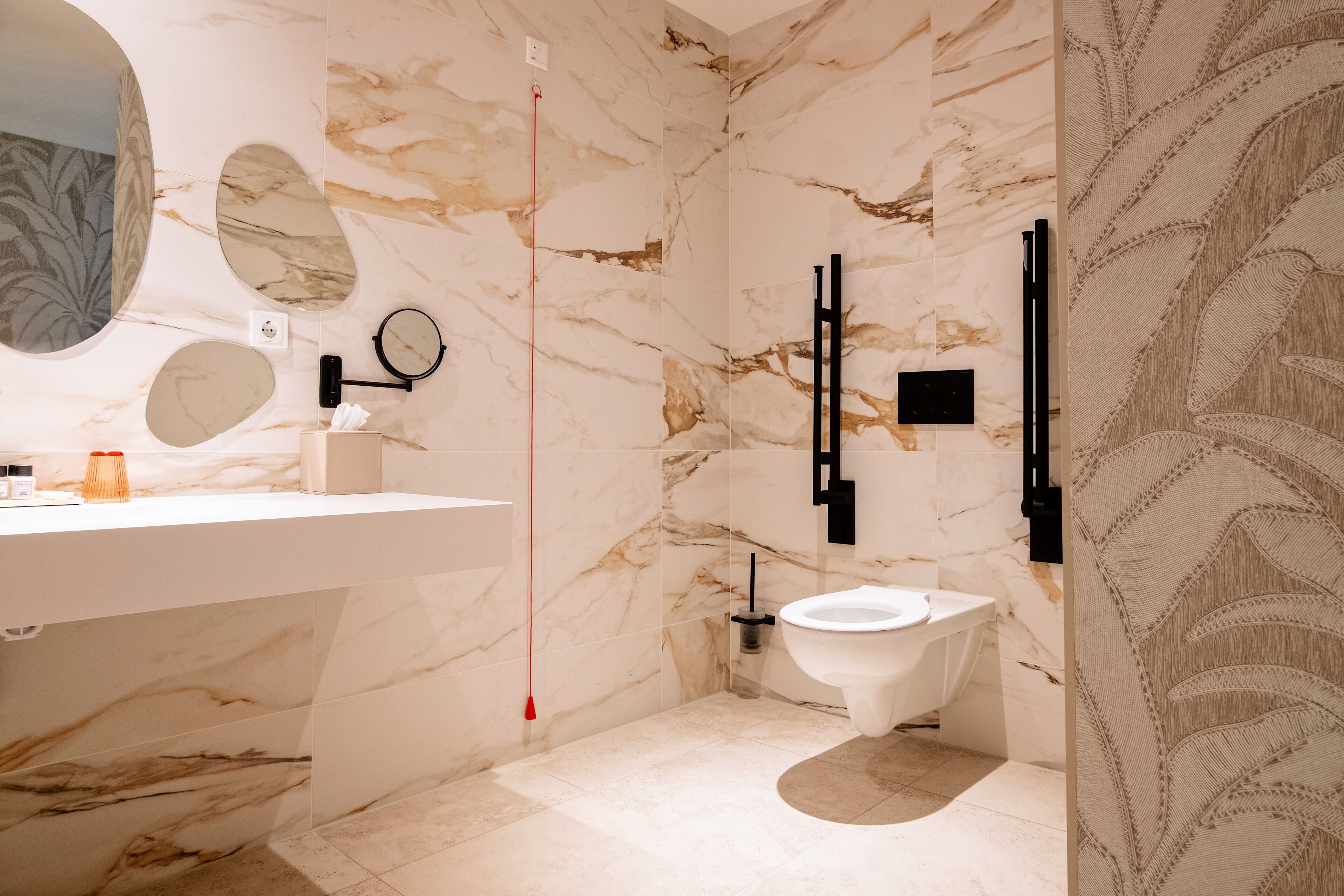 Une salle de bain moderne avec un mur en marbre, un miroir rond, des toilettes et un lavabo.