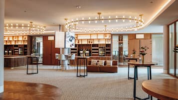 Een moderne hotel lobby met een houten receptiebalie, een zithoek met een bank en tafels, en een bar met flessen op de planken.