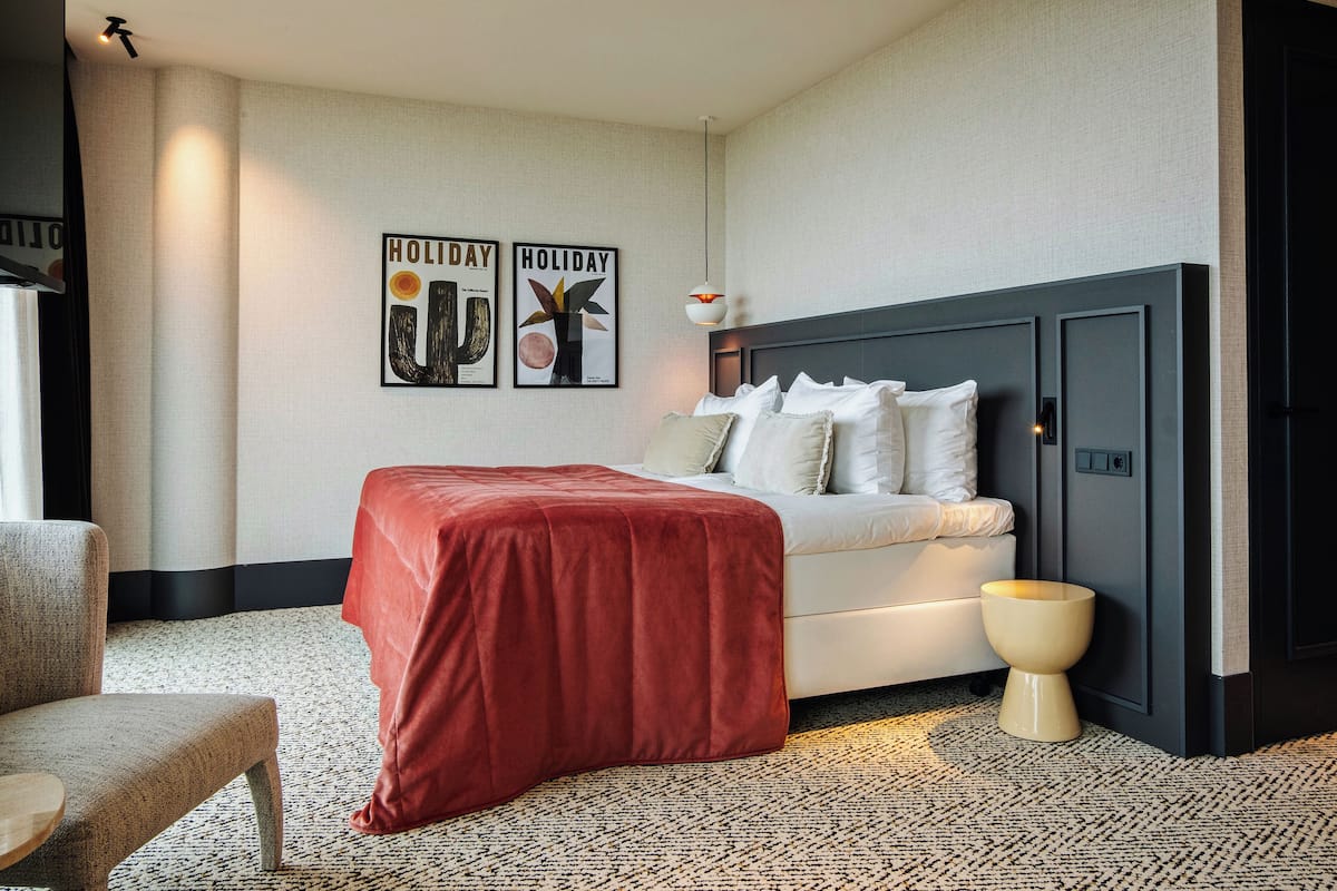 Une chambre d’hôtel moderne, équipée d’un lit, d’une chaise, d’une table de chevet et de deux tableaux encadrés accrochés au mur.