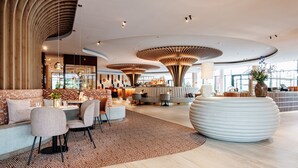 Un lobby moderno de hotel con una zona de estar central, un bar y una gran pieza decorativa blanca.