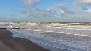 Een strand met golven en een bewolkte lucht.