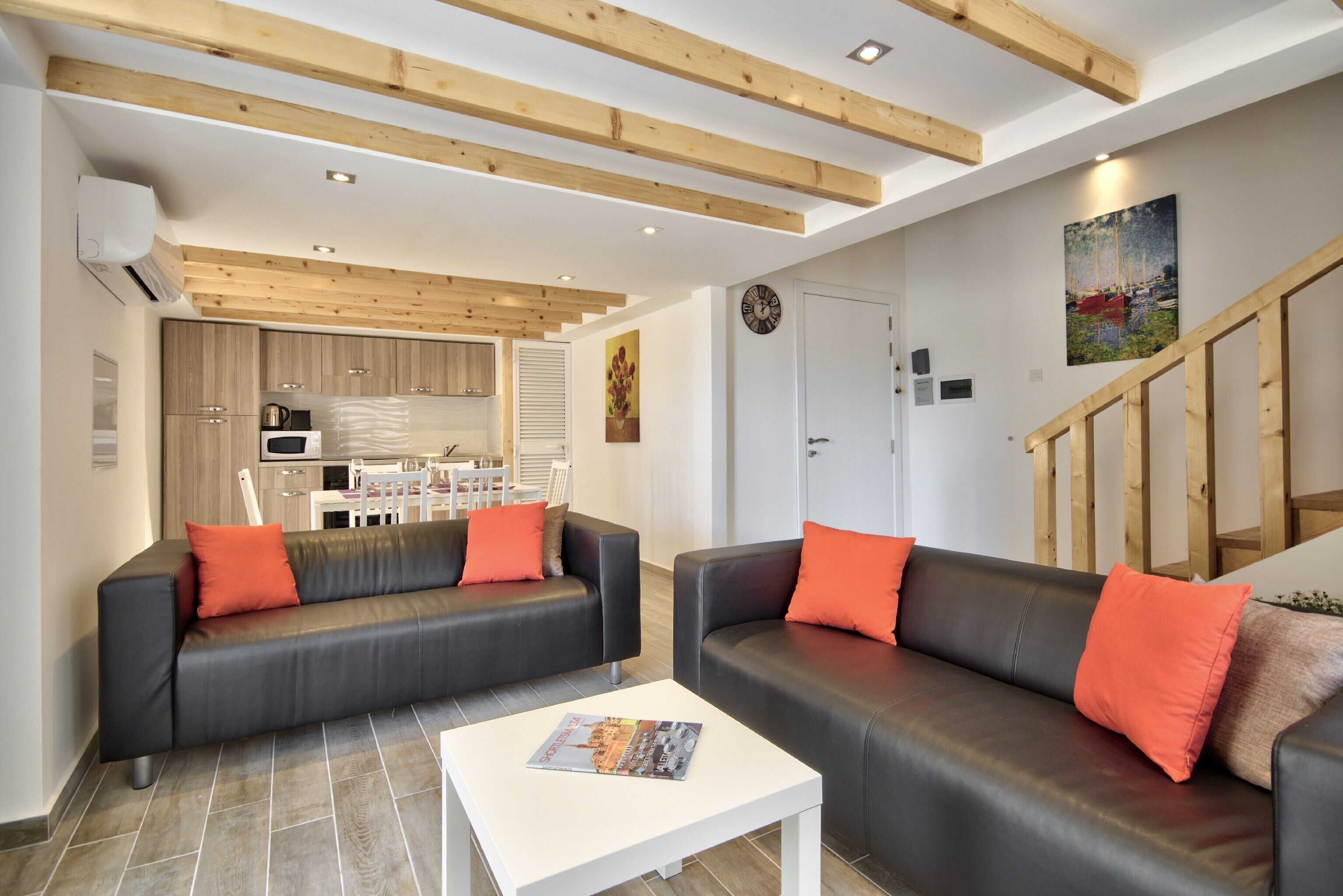 A modern living room with two black leather sofas, a white coffee table, and a wooden ceiling.