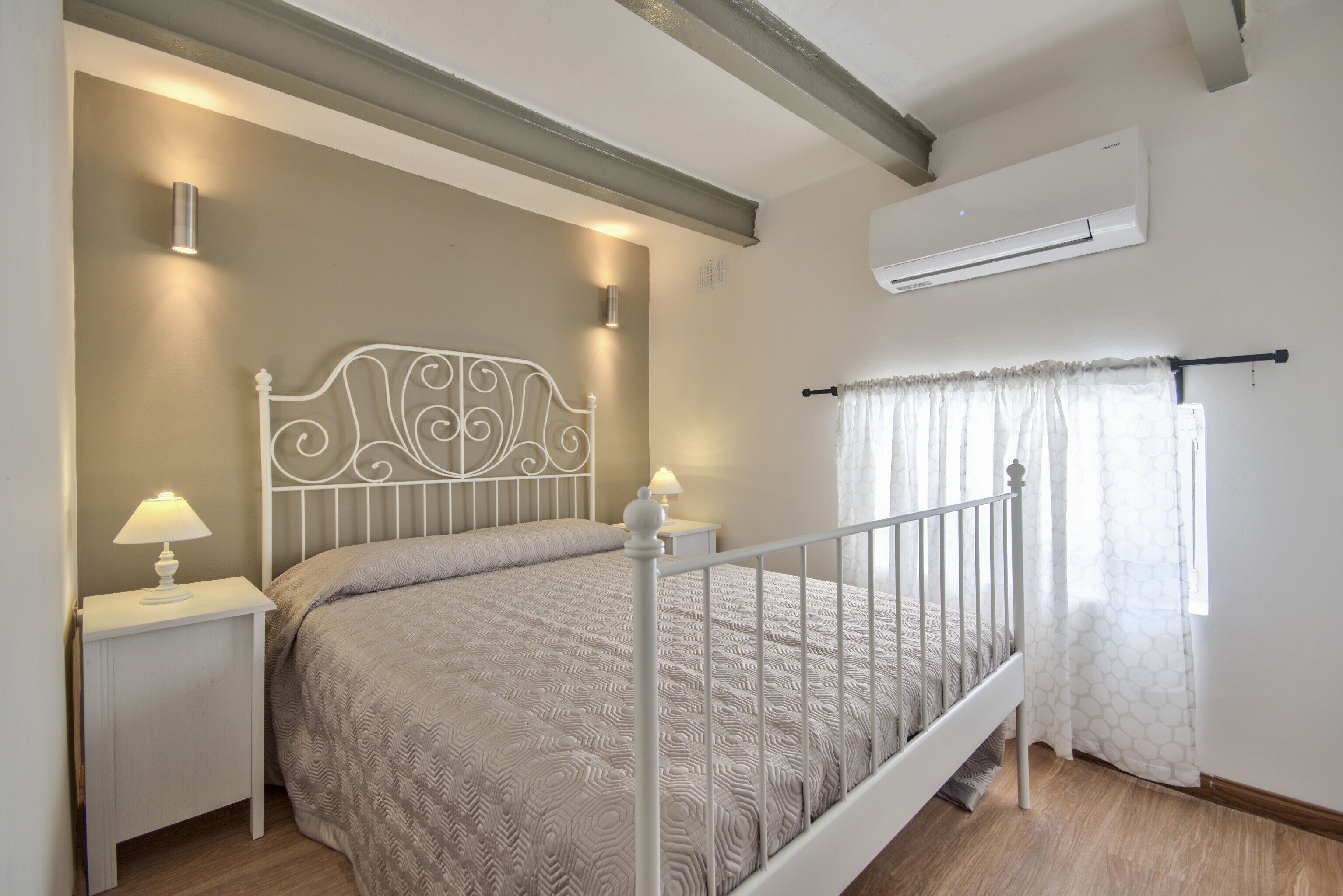 Une chambre à coucher comprenant un lit, des tables de chevet, un climatiseur et une fenêtre avec des rideaux.