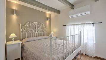 Une chambre à coucher comprenant un lit, des tables de chevet, un climatiseur et une fenêtre avec des rideaux.