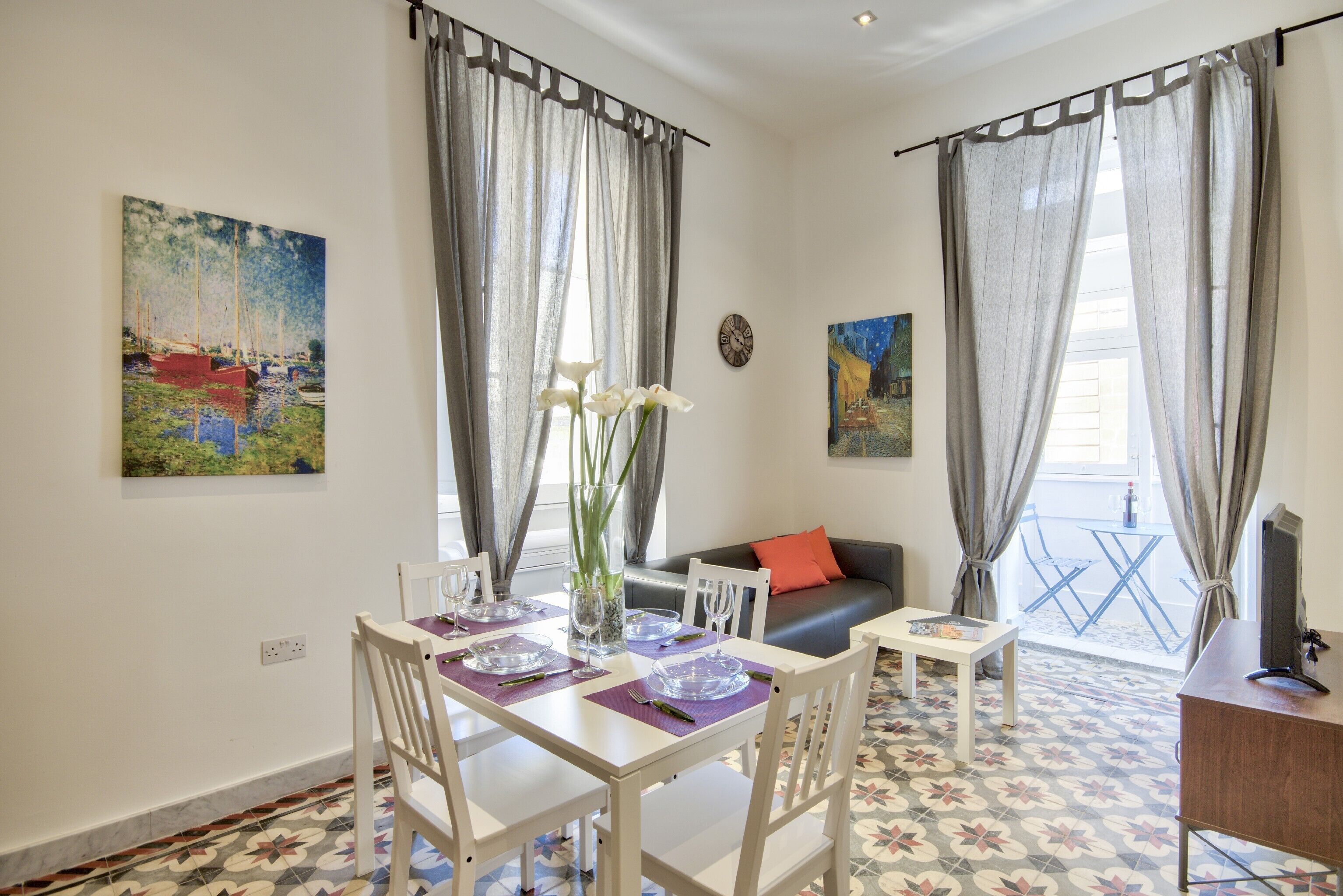 Un comedor con una mesa dispuesta para cuatro personas, un sofá y un mueble para la televisión.