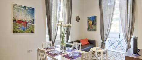 Un comedor con una mesa dispuesta para cuatro personas, un sofá y un mueble para la televisión.