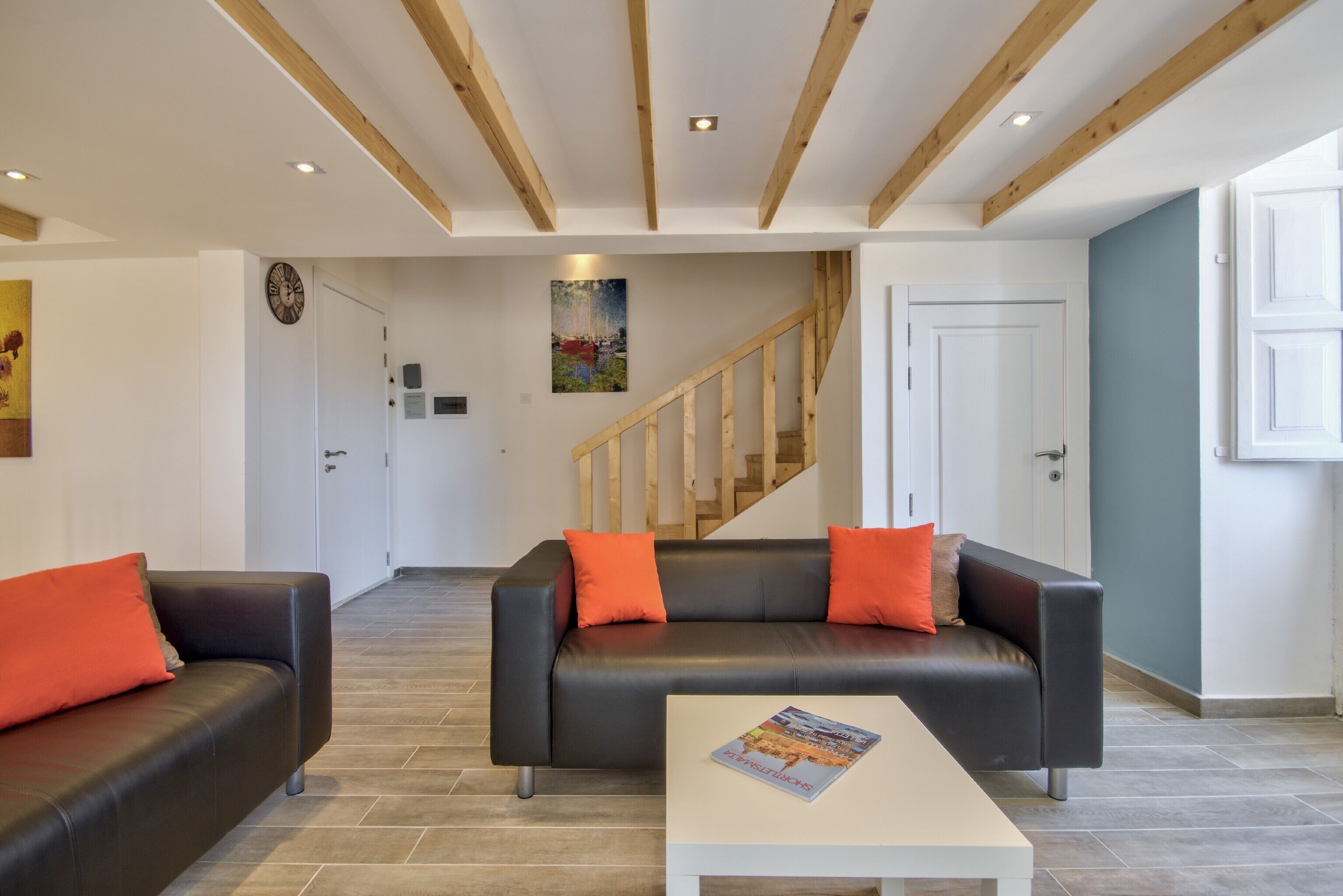 A modern living room with two black leather sofas, a white coffee table, and a staircase leading to another floor.