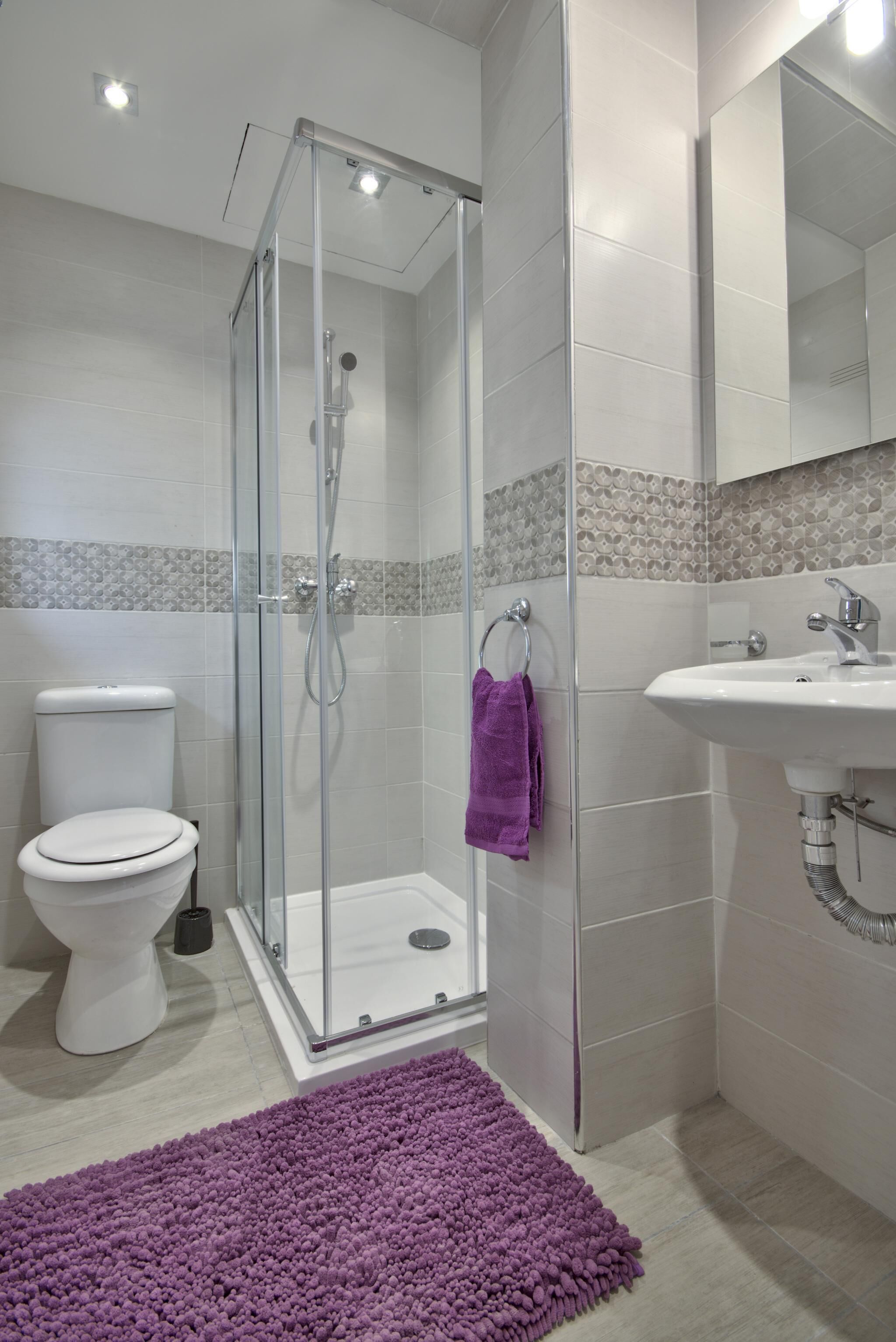 Un baño moderno con ducha de vidrio, inodoro blanco y lavamanos con espejo.