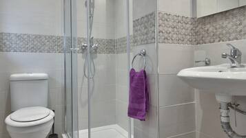 Un baño moderno con ducha de vidrio, inodoro blanco y lavamanos con espejo.