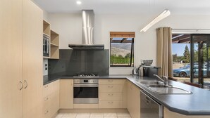 Een moderne keuken met een gasfornuis, oven en een roestvrijstalen afzuigkap. Er is een groot raam met uitzicht op een wijngaard en bergen.