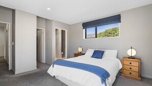Een slaapkamer met een bed, twee nachtkastjes, een raam met uitzicht en een deur naar een badkamer.