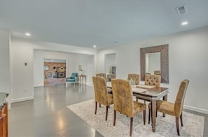 A spacious dining area with a large table and matching chairs, a patterned rug, and a decorative mirror on the wall.