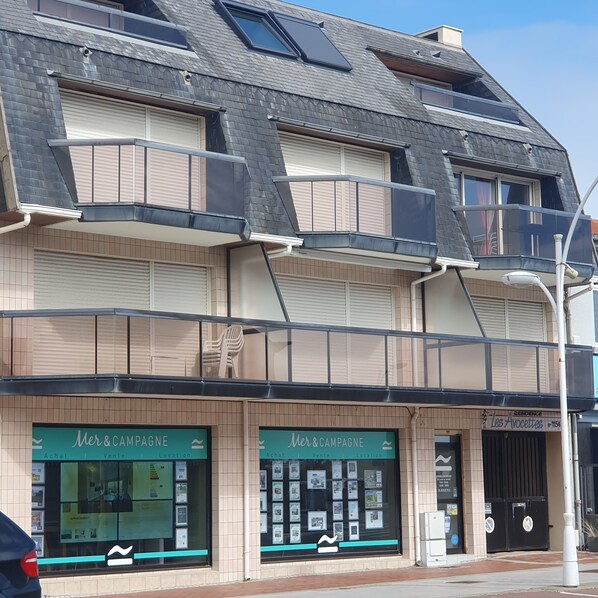 Un immeuble à plusieurs étages, doté d’une façade carrelée, de balcons et de devantures de magasins faisant la publicité de services immobiliers.
