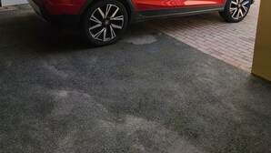 Ein roter SUV steht in einem überdachten Außenbereich mit geneigter Decke und einer weißen Wand mit farbigem Design.