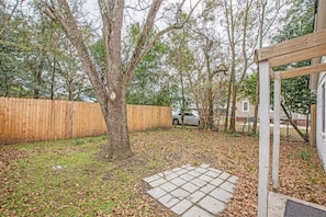 Un patio trasero con valla de madera, un árbol y una zona pavimentada.