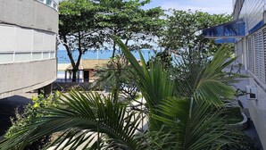 A building with a curved facade, a view of the sea, and lush greenery in the foreground. - 01E Vista Linda Pe Areia Guaruja - Tombo (Guarujá)