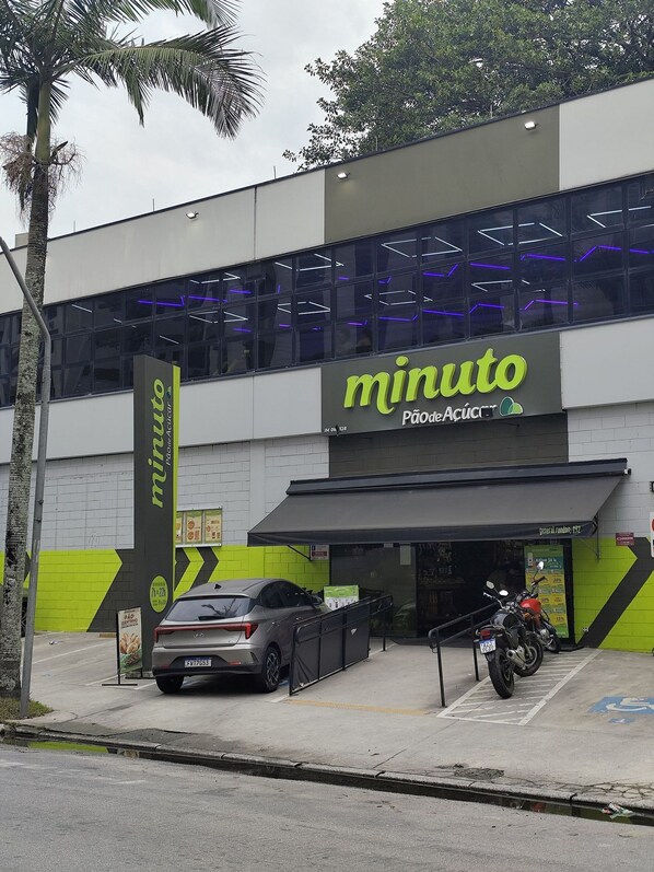Un edificio con un letrero que dice 'minuto Pão de Açúcar' y un estacionamiento con un auto y motocicletas.