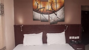 Habitació d'hotel amb un llit, dos coixins blancs, un capçal de fusta i una paret amb tres quadres abstractes.