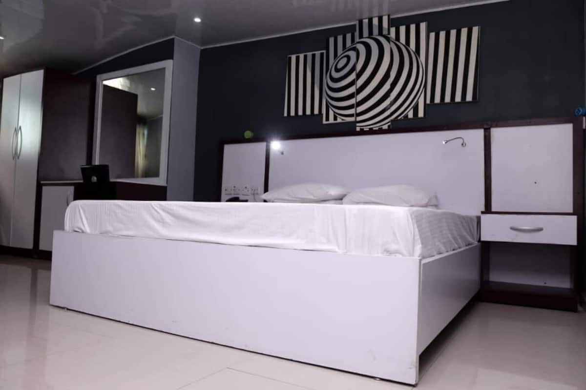 A modern bedroom with a white bed, a nightstand, a mirror, and abstract wall art.